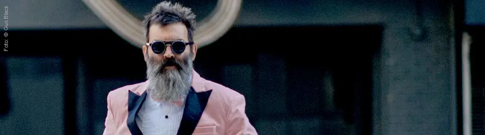 Ein Mann mit Bart in rosa Anzug und Sonnenbrille geht selbstbewusst nach vorne.