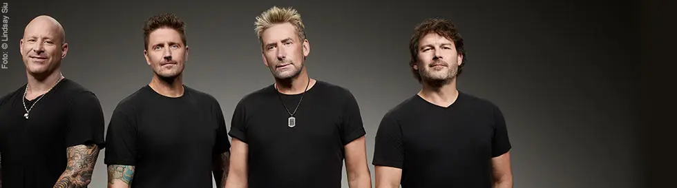 Vier Männer in schwarzen T-Shirts, frontal, neutraler Hintergrund.