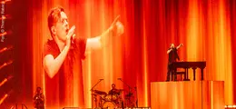 Ein Sänger auf einer Bühne mit Orchester davor, alles in orange Farben getaucht.