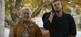 Ein älterer Mann und ein jüngerer Mann stehen nebeneinander, im Hintergrund Herbstbäume. 