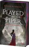 "Raven Kennedy: Played by the Piper. Die Unbeugsame. Roman. Eine Frau in rotem Kleid steht vor düsteren Bäumen."
