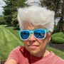 Text "WHY?" oben mittig. Person mit weißem Haar, bunter Sonnenbrille im grünen Park bei Sonnenschein.