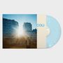 Text: "COLI"

Eine sonnige Stadtszene mit einem Menschen vor Gebäuden und einer blauen Vinyl-Schallplatte., LP