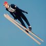 Die Zahl 58 auf einem Skispringer, der in der Luft schwebt. Der Himmel ist klar und blau., LP