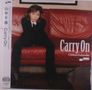 Text: „Carry On“, „Chihiro Yamanaka“. Eine Person sitzt in Anzug auf einem roten Sofa.