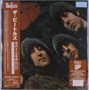 "The Beatles" und japanischer Text; drei Personen schauen zur Kamera, hinter Blättern versteckt, in dunkler Umgebung.