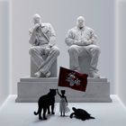 "Mégamarrons" steht auf einer Fahne. Zwei Statuen sitzen auf Podesten; ein Panther, ein Kind und eine Schildkröte davor.