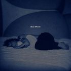 Text: "Blue Movie". Eine Person liegt in blauer Beleuchtung auf einem Bett, sie hält ein Kissen und hat Tattoos.