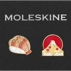 Der Text "MOLESKINE" steht oben. Darunter sind zwei bunte Anstecknadeln: links Sushi, rechts ein Berg vor Sonnenuntergang.