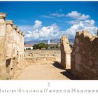 Ausgrabungen in Paphos. Alte Ruinen mit Säulen, blauer Himmel und Wolken im Hintergrund, sowie ein Leuchtturm in der Ferne.