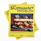 "UNSER BAUERNMARKT KOCHBUCH" steht oben auf einem gelben Buch mit einem Bild eines belegten Brots.