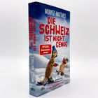 "Die Schweiz ist nicht genug" von Moritz Matthies. Zwei Erdmännchen fahren Ski, eines trägt eine blaue Mütze. SPIEGEL-Bestseller.
