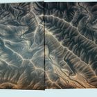 Ich erkenne keine Texte. Es zeigt eine Landschaft aus der Luft mit erodierten, verzweigten Mustern und Tälern.