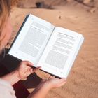 Ein Buch wird auf einem roten Handtuch in der Wüste gelesen. Texteinleitungen sind „Haltung ist kein Ideal“ und „Lektion #34: Landkarte“.