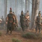 Krieger in antiker Rüstung marschieren durch einen nebeligen Wald, tragen Helme und Umhänge, wirken entschlossen.