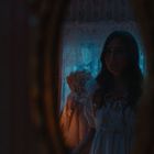 Eine unscharfe Spiegelung zeigt eine Frau in einem dunklen, stimmungsvoll beleuchteten Raum, umgeben von blauer Beleuchtung.