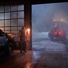 Text: "CASS COUNTY SHERIFF" auf einem Fahrzeug. Ein Traktor fährt aus einer offenen Garage in schneebedeckte Nacht.