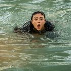 Eine Person schwimmt mit offenem Mund im Wasser. Sie trägt dunkle Kleidung.