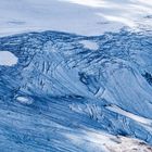 Eisige, wellenförmige Struktur mit blauen und weißen Schattierungen, die die Oberfläche eines Gletschers zeigt.