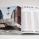 Text: "CRASH OUT", "Florentina Holzinger". Zwei Autos mit Graffiti und ein großer Kronleuchter hängen zwischen Gebäuden.