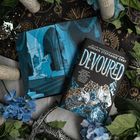 Ein Buch mit dem Titel "DEVOURERD" von Jordan Stephanie Gray. Es liegt auf einem offenen Buch mit einer blauen Zeichnung.