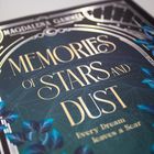 "Memories of Stars and Dust. Every Dream leaves a Scar." Verzierungen in Gold und Blau, sternenähnliche Muster.