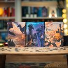 Ravensburger Puzzle. Drei Puzzle-Verpackungen mit Drachenmotiven auf einem Tisch, umgeben von Kerzen und Puzzleteilen.