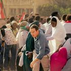 Menschenmenge bei einer Demonstration, viele mit farbigen Tüchern und Flaggen. Ein Mann im Vordergrund beugt sich vor.