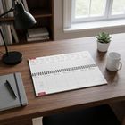 Kalender zeigt Woche vom 11. bis 17. Januar. Holztisch mit Lampe, Notizbuch, Stift, Tasse und Pflanze. Regal im Hintergrund.