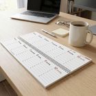 Kalenderblatt "Januar 2027" auf Holztisch, Laptop, Brille, Notizzettel, Kaffeetasse und Stift daneben.
