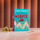 Buchtitel: "Murder at the Grand Alpine Hotel". Ein Buch auf einem Tisch mit einer goldenen Glocke und zwei Schlüsseln.