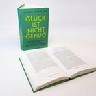 Ein Buch mit grünem Einband, darauf steht "GLÜCK IST NICHT GENUG. DIE RÜCKKEHR ZU EINEM ERFÜLLTEN LEBEN."