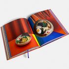 Farbiges Buch, aufgeschlagen mit zwei Seiten. Fotos von Ramen-Schüsseln auf buntem Hintergrund. Kein Text sichtbar.