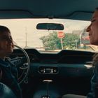 „STOP“-Schild draußen; zwei Menschen sitzen lächelnd in einem Auto, ein Kind links und eine Frau rechts.
