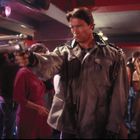 Ein Mann in einer Lederjacke zielt mit einer Waffe in einer belebten Bar oder einem Club.