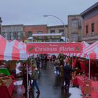 "The Annual Christmas Market" steht auf einem roten Schild mit weißen Buchstaben. Bunte Zelte und geschäftige Menschen.