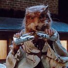 Text: "TOGRI". Eine Ratte in zerlumpter Kleidung hält ein zerbrochenes Metallrohr. Im Hintergrund ein beleuchtetes Gebäude.