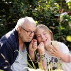 Ein älterer Mann und ein Kind sitzen im Garten. Beide halten Erdbeeren und das Kind macht ein Selfie.