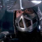 Ein Krieger in voller Rüstung mit Helm und Maske schaut aufmerksam, seine Rüstung glänzt im dunklen Hintergrund.