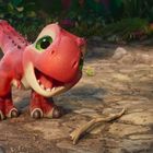 Ein fröhlicher, roter Baby-Dinosaurier mit großen Augen steht auf einem Erdboden, umgeben von bunten Blumen.