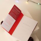 „BEFORE THE COFFEE GETS COLD“ steht auf einer Buchseite. Ein rotes Lesezeichen enthält weiteren Text. Lichter im Hintergrund.