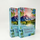 „AMELIA MARTIN“, „Töchter des Himalaya“, „ROMAN“. Zwei Bücher mit einem Himalaya-Motiv und blauen Blumen.