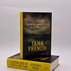 Buchcover mit Text: "WIE EIN FLUSS IN DER NACHT", darunter "TANA FRENCH". Buch steht auf einem liegenden Exemplar.
