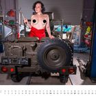 Kalenderseite März 2021. Frau mit rotem Tuch posiert vor altem Militärfahrzeug in einer Werkstatt.