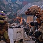 Ein Ninja Turtle mit lila Maske hält einen Kampfstab. Ihm gegenüber steht eine stachelige Kreatur in einer Werkstatt.