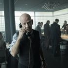 Ein älterer Mann telefoniert in einem Büro, wo mehrere Menschen beschäftigt sind.
