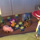 Eine Figur mit rotem Hut steht vor Spielzeugfiguren: Dinosaurier, Schwein, Aliens und Einhorn in einem Kinderzimmer.