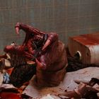Blutige Szene mit zersplittertem Porzellan; eine Kreatur mit scharfen Zähnen und Krallen ragt aus einem Chaos hervor.