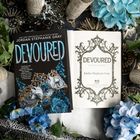 Buchcover mit "DEVOURD" in großen, blauen Buchstaben, umgeben von blauen Blumen und einem dekorativen Muster.