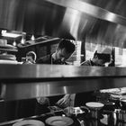 Köche arbeiten konzentriert in einer Restaurantküche, umrundet von Töpfen und Tellern auf der Arbeitsfläche.